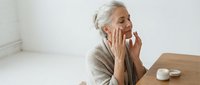 Senior Caucasian woman applying anti-aging skincare cream to face in modern bathroom. Mature female enjoying daily beauty routine and self-care ritual.