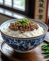 Ground meat with green onions served over steamed white rice in traditional blue and white porcelain bowl, garnished with fresh chili peppers on wooden table.