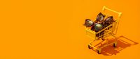 Miniature shopping cart filled with walnuts on vibrant orange background, representing online grocery shopping, e-commerce, and food retail concepts.