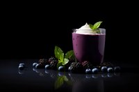Purple berry smoothie with whipped cream and mint garnish surrounded by fresh blueberries and blackberries on dark background for healthy lifestyle.