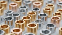 Rows of metallic cylindrical components in gold, silver, and copper colors arranged in precise pattern for industrial manufacturing.