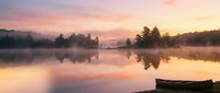 Serene lake at sunrise with mist rising from calm water, evergreen trees silhouetted against pink and golden sky, wooden boat in foreground. Nature landscape.