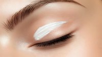 Close-up macro shot of closed eye with white cream eyeshadow makeup and long eyelashes. Professional beauty cosmetics application on smooth skin.