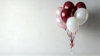Elegant bunch of burgundy, pearl pink and white helium balloons tied with ribbon against neutral wall background, creating minimalist festive mood.