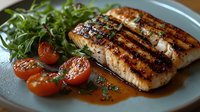 Grilled salmon fillet with caramelized glaze served alongside fresh arugula salad and roasted cherry tomatoes on gray ceramic plate with sauce reduction.