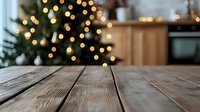 Rustic wooden table surface with blurred Christmas tree and warm bokeh lights in background, creating cozy holiday atmosphere in modern kitchen interior.