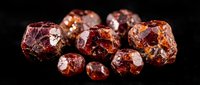 Raw red garnet gemstones collection with natural crystalline structure and deep burgundy color tones on black background for jewelry making and mineral study.