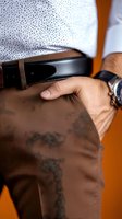 Close-up view of man's casual business attire showing hand in pocket of brown chinos, black leather belt, patterned shirt and wristwatch against orange background.