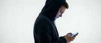 Young Caucasian man in black hoodie using smartphone against white background, side profile view for technology and communication concepts.