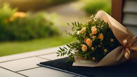 Delicate spray roses wrapped in kraft paper with satin bow lying on dark textile surface against blurred garden background, romantic floral arrangement in warm tones.
