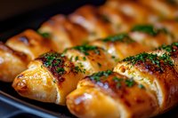 Freshly baked bread rolls with herbs and garlic butter glaze on dark baking sheet, close-up view showing golden brown crust and aromatic seasoning.