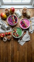 Colorful smoothie bowls with fresh berries, nuts and seeds arranged on wooden table near window for healthy breakfast meal preparation and nutrition concept.