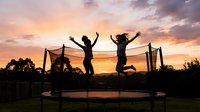 Silhouettes of two children jumping on trampoline at sunset with dramatic sky, outdoor recreational activity for kids, leisure and fun.