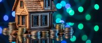 Miniature wooden house model surrounded by stacks of golden coins with colorful bokeh lights background for real estate investment concepts.