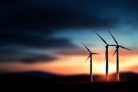 Wind turbines silhouetted against dramatic sunset sky with dark clouds and orange horizon, representing renewable energy and sustainable power generation.