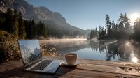 Laptop and coffee cup on wooden dock overlooking misty mountain lake at sunrise, remote work and digital nomad lifestyle concept.
