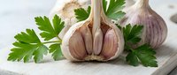 Fresh garlic bulbs with green parsley herbs on wooden cutting board for cooking and culinary preparations in kitchen setting.