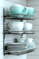 Organized kitchen cabinet with mint green and white ceramic dishes, cups and plates on chrome wire shelving racks for modern home storage solutions.