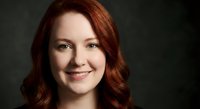 Professional headshot of smiling Caucasian woman with red hair against dark background for corporate branding and marketing materials.