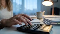 Professional woman calculating finances on calculator at modern office desk with warm lighting and documents for business accounting tasks.