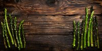 Fresh green asparagus spears arranged on rustic wooden background, creating natural frame for food photography or menu design.