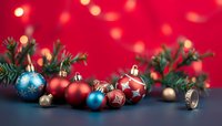 Festive Christmas ornaments in red and blue with pine branches against vibrant red bokeh background for holiday decorating.