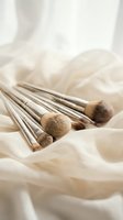 Luxury makeup brushes with silver handles arranged on soft cream silk fabric, elegant beauty tools collection for cosmetics and skincare content.