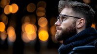 Man with beard and glasses in profile wearing dark sweater against warm bokeh lights, suitable for lifestyle, portrait, and advertising campaigns.