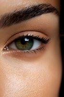 Close-up of a green eye with long eyelashes and defined eyebrow showing professional makeup application. Glowing skin with subtle shimmer highlights beauty look.