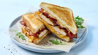 Grilled bacon egg cheese sandwich on toasted bread served on white plate with fresh greens for breakfast or lunch meal.