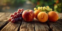 Fresh seasonal fruits arranged on rustic wooden table with natural lighting, showcasing red apple, peach, orange and grapes for healthy eating concept.