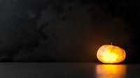 Glowing orange pumpkin on dark background with dramatic lighting creates spooky Halloween atmosphere, illuminated from within against black backdrop.