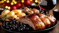 Juicy roasted pork belly with crispy skin served on black plate with olives, red wine glass and festive bokeh lights in background. Holiday dinner setting.