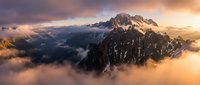 Dramatic mountain peaks emerging through golden clouds at sunrise, alpine landscape with warm light and misty atmosphere for nature and travel content.
