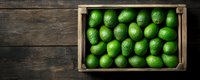 Fresh green limes arranged in rustic wooden crate on dark wooden background, top view. Raw organic citrus fruits for cooking and beverages.