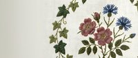 Vintage botanical embroidery featuring ivy vine, pink roses and blue cornflowers on cream fabric. Traditional needlework floral design for home decor projects.
