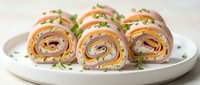 Sliced tortilla wraps filled with ham, cheese, and fresh vegetables arranged on a white plate, ready to serve as appetizers or lunch.