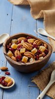 Wooden bowl filled with mixed nuts, dried cranberries and candied ginger on rustic blue table with burlap cloth for healthy snacking and cooking.