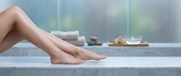 Smooth bare legs of a young woman resting on a marble surface in a spa setting with towels and wellness accessories in the background.
