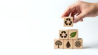 Hand placing wooden cube with recycling symbol on pyramid of eco-friendly blocks featuring green energy and environmental sustainability icons.