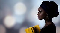 African woman in traditional headwrap holding yellow folders in profile view against blurred city lights background for business and professional concepts.
