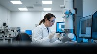 Female scientist in white lab coat working with microscope in modern research laboratory for medical analysis and scientific discovery.