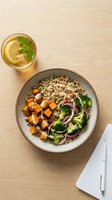 Healthy grain bowl with roasted sweet potato, broccoli, red onion and tahini dressing, served with lemon iced tea on a wooden table.
