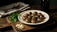 Homemade meatballs on white plate with fresh parsley and garlic on rustic wooden table. Traditional comfort food for family dinner and cooking blogs.