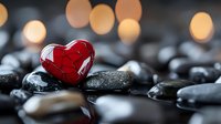Red glass heart resting on smooth black spa stones with warm bokeh lights creating romantic wellness atmosphere for Valentine's Day relaxation concepts.