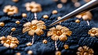 Delicate golden floral embroidery on dark blue fabric with embroidery needle in process, showing intricate handmade needlework details and craftsmanship.