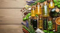 Natural essential oils in glass bottles with fresh herbs, spices and aromatherapy ingredients arranged on rustic wooden background for wellness and spa treatments.