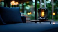 Atmospheric glass lantern with warm glowing light on wooden table against dark blue sofa, creating cozy evening ambiance with bokeh background.