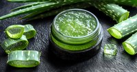 Fresh aloe vera gel in glass jar with cut pieces of natural plant on black stone background, organic skincare and wellness concept for spa treatments.