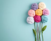 Creative composition of colorful yarn balls arranged as flower blooms with green knitted leaves on pastel blue background, crafting and knitting concept.